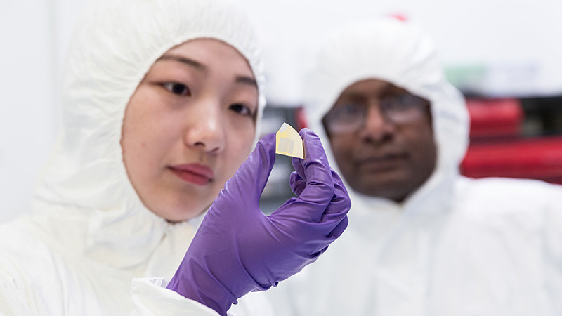 Student and technician in clean room suits holding up an LED to the camera